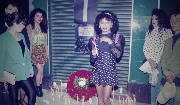 Imagen de primera manifestación LGBT en Guatemala en memoria de Conchita Alonso. Se ve una activista con una vela prendida y de fondo más velas prendidas y un altar de flores.